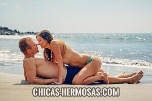 Relaciones exclusivas: En la imagen vemos una pareja teniendo un momento apasionado. Están disfrutando de un día de playa. Mientras él esta acostado sobre su espalda, ella está sobre el acercándose para darle un beso.