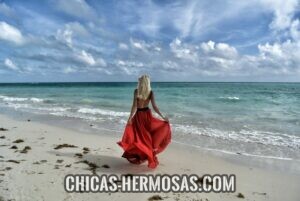 Mujeres hermosas: Mujer hermosa caminando en un vestido rojo por la playa. Un ejemplo de Sugar Baby.